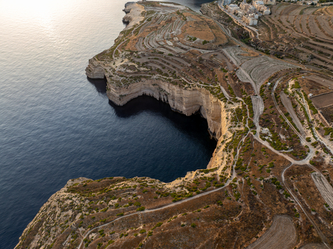 Aerial view of rugged cliffs plunging into the deep blue sea where the terraced landscape meets the coastal edge Munxar Gozo Malta. Aerial view of rugged cliffs plunging into the deep blue sea where the terraced landscape meets the coastal edge Munxar Gozo Malta.