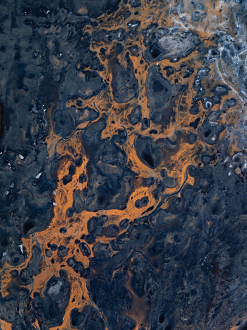 Aerial view of the intricate patterns of dark volcanic rock and vibrant orange mineral deposits across the rugged landscape of Iceland. Aerial view of the intricate patterns of dark volcanic rock and vibrant orange mineral deposits across the rugged landscape of Iceland.