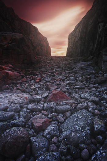 View of a rocky valley filled with large boulders between steep cliffs under a dramatic sunset sky in Sweden.
