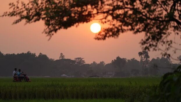 View of a sunset over rural fields with people on a bike Bangladesh. View of a sunset over rural fields with people on a bike Bangladesh.