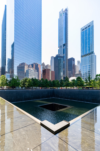 View of the 911 Memorial reflecting pool surrounded by modern skyscrapers and lush green trees in New York New York United States. View of the 911 Memorial reflecting pool surrounded by modern skyscrapers and lush green trees in New York New York United States.