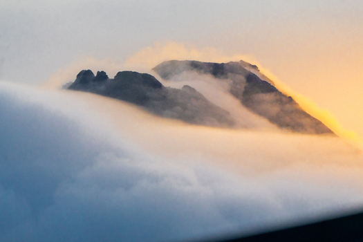 View of a mountain peak rising above a thick layer of clouds during golden hour in Costa Rica.