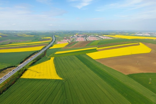 Aerial view of vibrant yellow canola and green agricultural fields with a highway and distant buildings under a blue sky Silivri Istanbul Turkey. Aerial view of vibrant yellow canola and green agricultural fields with a highway and distant buildings under a blue sky Silivri Istanbul Turkey.