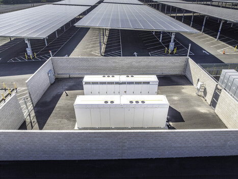 Aerial view of Tesla Megapack battery storage units enclosed by a wall next to solar panel carports at Six Flags Magic Mountain Los Angeles County California United States. Aerial view of Tesla Megapack battery storage units enclosed by a wall next to solar panel carports at Six Flags Magic Mountain Los Angeles County California United States.