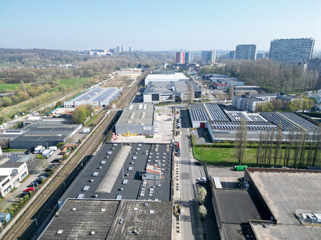 Aerial view of rooftops shimmering under the sunlight industrial buildings standing tall amidst the urban landscape and green spaces providing a serene backdrop Ganshoren Brussels Belgium. Aerial view of rooftops shimmering under the sunlight industrial buildings standing tall amidst the urban landscape and green spaces providing a serene backdrop Ganshoren Brussels Belgium.