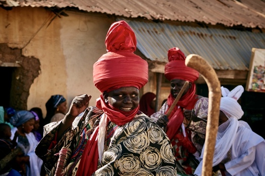 Zaria city Nigeria 21 March 2026 View of a vibrant figure in a red turban and patterned robe smiling amidst a warm textured local backdrop. Zaria city Nigeria 21 March 2026 View of a vibrant figure in a red turban and patterned robe smiling amidst a warm textured local backdrop.