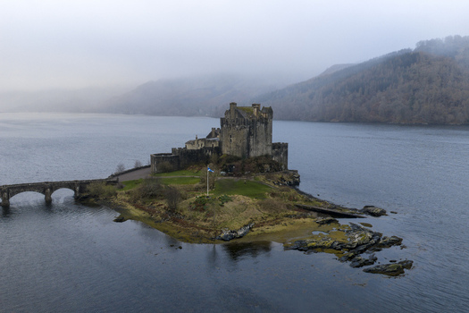 Aerial view of Eilean Donan Castle on its tidal island with the stone bridge and misty Highland hills in Dornie Scotland United Kingdom.