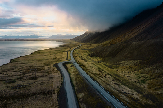 Aerial view of Vestrahorn mountain and the coastal road winding through the dramatic landscape of Iceland during golden hour with dark clouds overhead Sveitarfelagid Hornafjordur Iceland. Aerial view of Vestrahorn mountain and the coastal road winding through the dramatic landscape of Iceland during golden hour with dark clouds overhead Sveitarfelagid Hornafjordur Iceland.