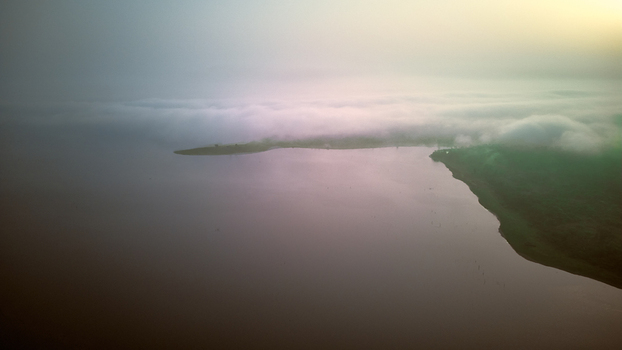 Aerial view of the calm waters of Owala Reservoir shrouded in morning mist under a soft golden sky in Osogbo Osun Nigeria. Aerial view of the calm waters of Owala Reservoir shrouded in morning mist under a soft golden sky in Osogbo Osun Nigeria.