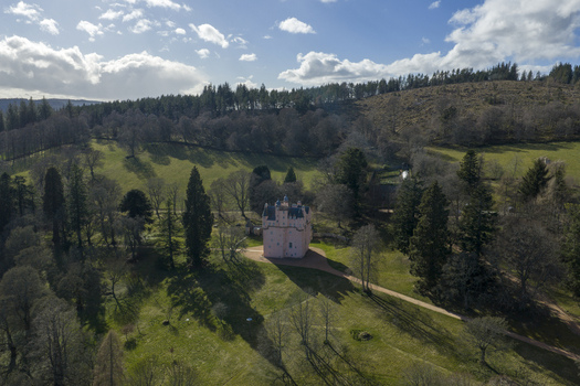 Aerial view of the pink Craigievar Castle surrounded by lush green lawns and dense woodland under a bright sky Craigievar Scotland United Kingdom.