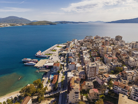 Aerial view of Saranda harbor with ferries docked along the pier surrounded by urban buildings and the blue Ionian Sea in Saranda Vlore County Albania. Aerial view of Saranda harbor with ferries docked along the pier surrounded by urban buildings and the blue Ionian Sea in Saranda Vlore County Albania.
