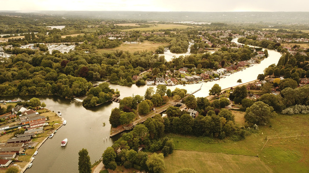Aerial view of the Thames River winding through lush green countryside with residential houses moored boats and dense trees in Thames United Kingdom. Aerial view of the Thames River winding through lush green countryside with residential houses moored boats and dense trees in Thames United Kingdom.