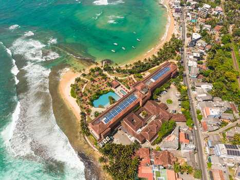 Aerial view of a large beachfront resort with a swimming pool and palm trees along the turquoise coastline in Hikkaduwa Southern Province Sri Lanka. Aerial view of a large beachfront resort with a swimming pool and palm trees along the turquoise coastline in Hikkaduwa Southern Province Sri Lanka.