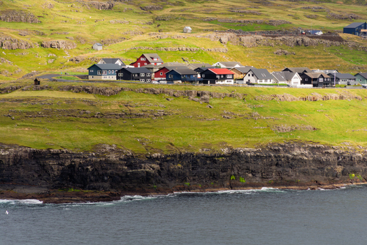 View of colorful houses perched on a grassy cliff overlooking the rugged coastline and sea in the Faroe Islands.