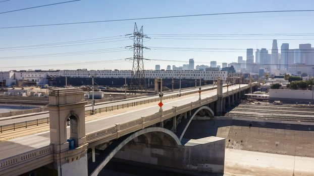Aerial view of the 6th Street Viaduct with concrete arches and the Los Angeles skyline in the background featuring railway tracks and power lines in Los Angeles California United States.