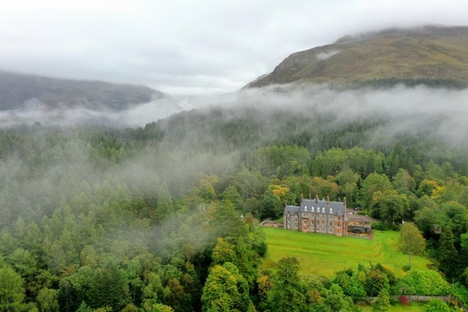 Aerial view of a historic stone building nestled in the lush misty forests of Glencoe Scotland United Kingdom.