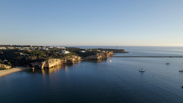 Aerial view of the Ferragudo coastline featuring the lighthouse rocky cliffs calm blue sea and sailboats in the bay Ferragudo Faro District Portugal.