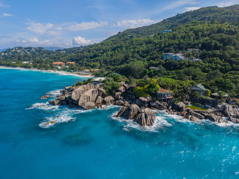 Aerial view of turquoise waters meeting the rocky coastline lush hills dotted with homes creating a vibrant contrast of blues and greens La Retraite Mahe Island Seychelles. Aerial view of turquoise waters meeting the rocky coastline lush hills dotted with homes creating a vibrant contrast of blues and greens La Retraite Mahe Island Seychelles.