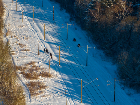 Aerial view of people riding horses along snowy railway tracks and power lines through a winter forest landscape Lithuania. Aerial view of people riding horses along snowy railway tracks and power lines through a winter forest landscape Lithuania.