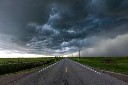View of a long straight road stretching into the distance under a dramatic and heavy dark storm cloud formation over the green landscape in Oklahoma City Oklahoma United States.