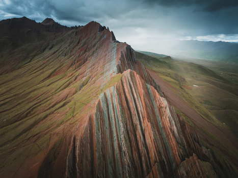 Aerial view of Pallay Punchu Rainbow Mountain with its distinctive colorful striped rock formations under a dramatic cloudy sky in Layo Cuzco Peru.