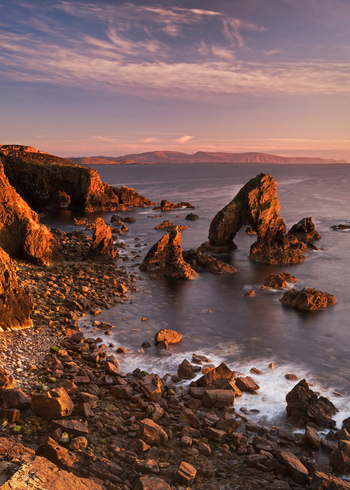 View of Crohy Head Sea Arch and jagged rock formations along the rugged coastline under a warm sunset sky County Donegal Ireland. View of Crohy Head Sea Arch and jagged rock formations along the rugged coastline under a warm sunset sky County Donegal Ireland.