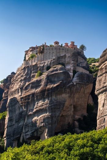 Aerial view of the historic Meteora monasteries perched atop massive sandstone rock formations surrounded by lush greenery under a clear blue sky in Trikala Greece. Aerial view of the historic Meteora monasteries perched atop massive sandstone rock formations surrounded by lush greenery under a clear blue sky in Trikala Greece.