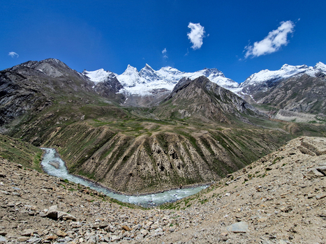 View of the Penzi La road winding through the rugged mountain landscape of the Zanskar valley featuring snow capped peaks a glacial river and rocky slopes in Zanskar Ladakh India.