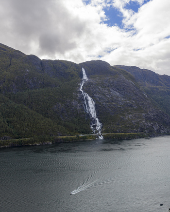 Aerial view of Langfossen waterfall cascading down a steep mountain into the Akrafjorden with a small boat on the water Fjaera Vestland Norway. Aerial view of Langfossen waterfall cascading down a steep mountain into the Akrafjorden with a small boat on the water Fjaera Vestland Norway.