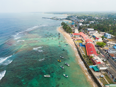 Aerial view of the turquoise coastline with coral reefs sandy beaches and numerous small boats anchored near the shore in Hikkaduwa Southern Province Sri Lanka. Aerial view of the turquoise coastline with coral reefs sandy beaches and numerous small boats anchored near the shore in Hikkaduwa Southern Province Sri Lanka.