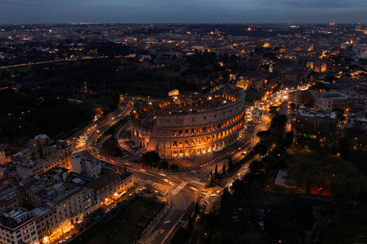 Roma Italy 06 April 2022 Aerial view of the Colosseum illuminated at night surrounded by the historic urban landscape of Rome with glowing street lights and traffic trails. Roma Italy 06 April 2022 Aerial view of the Colosseum illuminated at night surrounded by the historic urban landscape of Rome with glowing street lights and traffic trails.