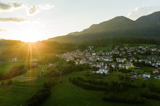Aerial view of Fiemme Valley with a charming village nestled among lush green fields and mountains under the warm glow of the setting sun in Trentino Alto Adige Italy.