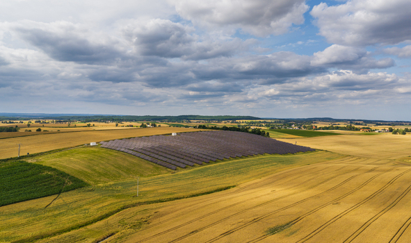 Aerial view of a solar farm situated in the middle of golden agricultural fields under a cloudy sky in Tczew Pomeranian Voivodeship Poland. Aerial view of a solar farm situated in the middle of golden agricultural fields under a cloudy sky in Tczew Pomeranian Voivodeship Poland.