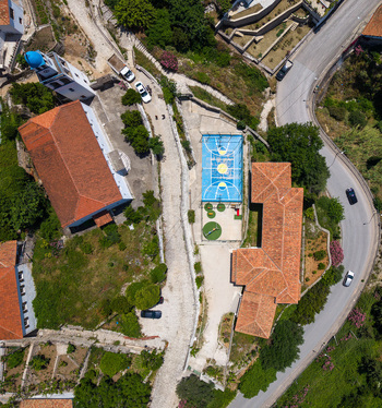 Aerial view of a blue basketball court and a church with a blue dome among terracotta rooftops and winding roads in Dhermi Vlore County Albania.
