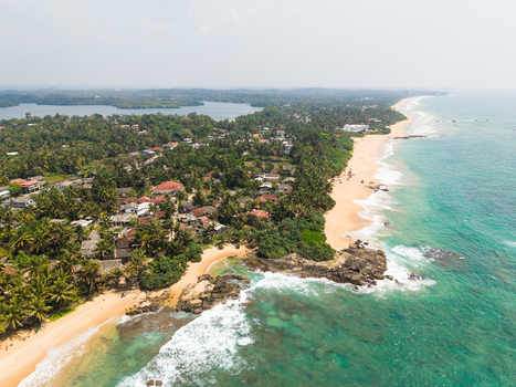Aerial view of the tropical coastline with sandy beaches turquoise ocean waves and lush palm trees surrounding residential houses Dodanduwa Southern Province Sri Lanka. Aerial view of the tropical coastline with sandy beaches turquoise ocean waves and lush palm trees surrounding residential houses Dodanduwa Southern Province Sri Lanka.