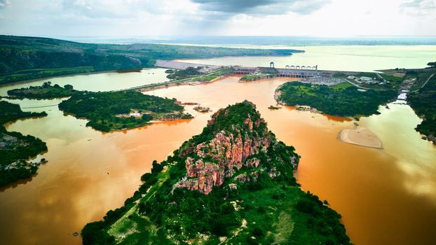 Aerial view of the Jebba Dam on the Niger River featuring a prominent rocky outcrop in the foreground lush green vegetation and the expansive reservoir in Jebba Niger Nigeria.