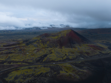Aerial view of a dramatic landscape where a lone vehicle traces a path through dark volcanic earth under a sky heavy with brooding clouds Snæfellsnes Iceland. Aerial view of a dramatic landscape where a lone vehicle traces a path through dark volcanic earth under a sky heavy with brooding clouds Snæfellsnes Iceland.