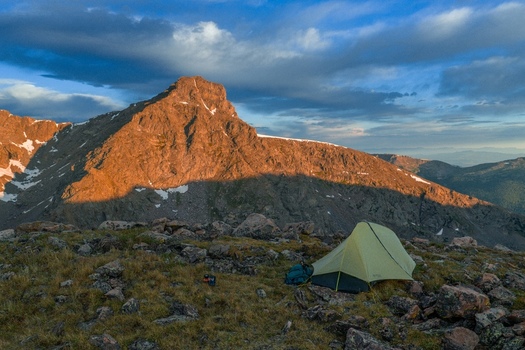 Aerial view of a tent pitched on a rocky mountain slope with Mount of the Holy Cross illuminated by golden hour light in the Sawatch Range Vail Colorado United States. Aerial view of a tent pitched on a rocky mountain slope with Mount of the Holy Cross illuminated by golden hour light in the Sawatch Range Vail Colorado United States.