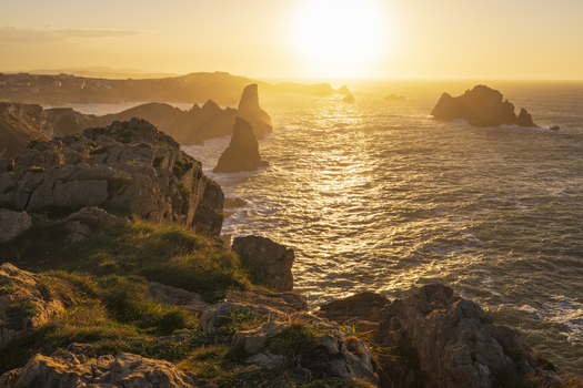 View of the rugged coastline and sea stacks under a golden sunset with waves crashing against rocky cliffs in Liencres Cantabria Spain. View of the rugged coastline and sea stacks under a golden sunset with waves crashing against rocky cliffs in Liencres Cantabria Spain.