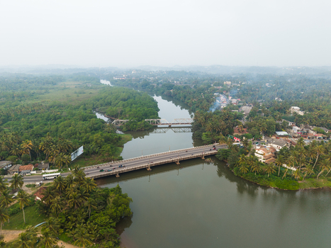 Aerial view of the Gin Ganga river with road and railway bridges surrounded by lush tropical palm trees and residential buildings in Galle Southern Province Sri Lanka.