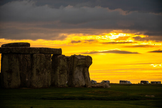 View of Stonehenge at sunset with dramatic golden light illuminating the ancient megalithic stones and the surrounding landscape in Salisbury England United Kingdom.