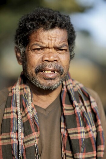 Odisha India 26 March 2026 View of a man with weathered skin and furrowed brow wearing a brown shirt and a colorful plaid scarf stands against a blurred background. Odisha India 26 March 2026 View of a man with weathered skin and furrowed brow wearing a brown shirt and a colorful plaid scarf stands against a blurred background.