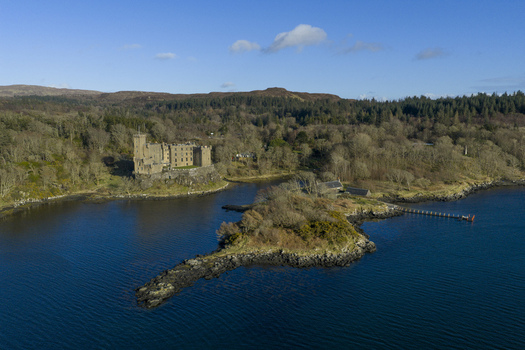 Aerial view of Dunvegan Castle and Gardens perched on a rocky cliff overlooking the blue waters of Loch Dunvegan and surrounded by lush woodland Isle of Skye Scotland United Kingdom. Aerial view of Dunvegan Castle and Gardens perched on a rocky cliff overlooking the blue waters of Loch Dunvegan and surrounded by lush woodland Isle of Skye Scotland United Kingdom.