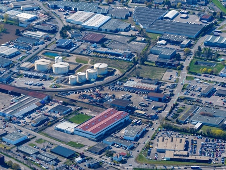 Aerial view of a sprawling industrial landscape dotted with silver storage tanks and large warehouses under a clear sky Sausheim Grand Est France.