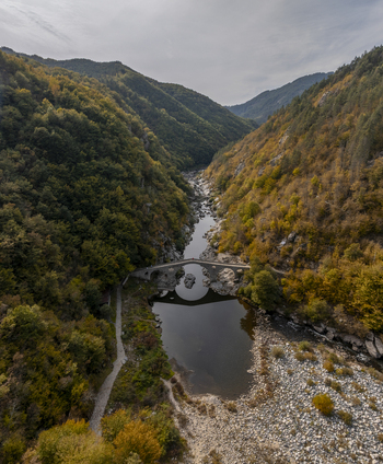 Aerial view of Devil s Bridge spanning the Arda River amidst autumn colored forests and rocky slopes in Kardzhali Province Bulgaria. Aerial view of Devil s Bridge spanning the Arda River amidst autumn colored forests and rocky slopes in Kardzhali Province Bulgaria.
