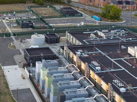 Aerial view of a modern data center facility featuring rooftop HVAC units industrial infrastructure security fencing and a parking area in the United Kingdom. Aerial view of a modern data center facility featuring rooftop HVAC units industrial infrastructure security fencing and a parking area in the United Kingdom.