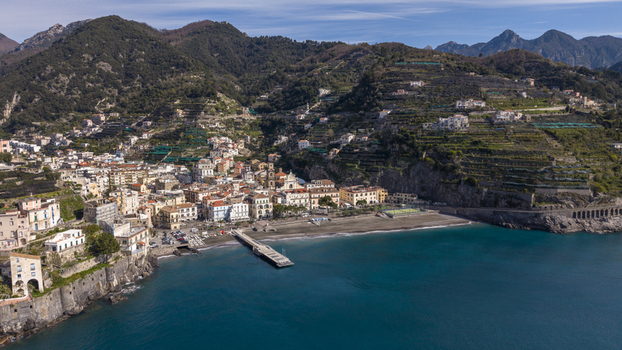 Aerial view of the colorful buildings nestled between the mountains and the sea with a long pier extending into the blue water Minori Campania Italy. Aerial view of the colorful buildings nestled between the mountains and the sea with a long pier extending into the blue water Minori Campania Italy.