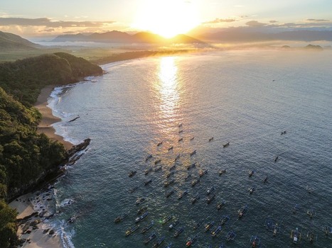 Aerial view of Papuma Beach with traditional fishing boats on the calm sea during a golden sunrise with lush coastal cliffs and sandy shores in Jember East Java Indonesia. Aerial view of Papuma Beach with traditional fishing boats on the calm sea during a golden sunrise with lush coastal cliffs and sandy shores in Jember East Java Indonesia.