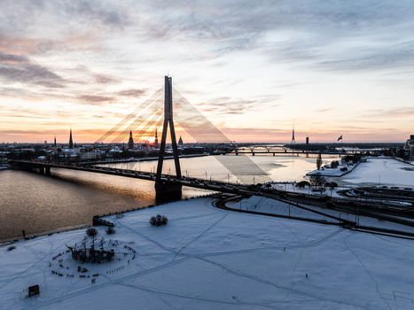 Aerial view of the Vansu Bridge spanning the Daugava river with snow covered banks and the city skyline at sunset in Riga Latvia.
