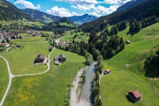 Aerial view of the Sarine river flowing through a valley with traditional wooden barns and lush green meadows surrounded by dense pine forests in Rougemont Vaud Switzerland. Aerial view of the Sarine river flowing through a valley with traditional wooden barns and lush green meadows surrounded by dense pine forests in Rougemont Vaud Switzerland.